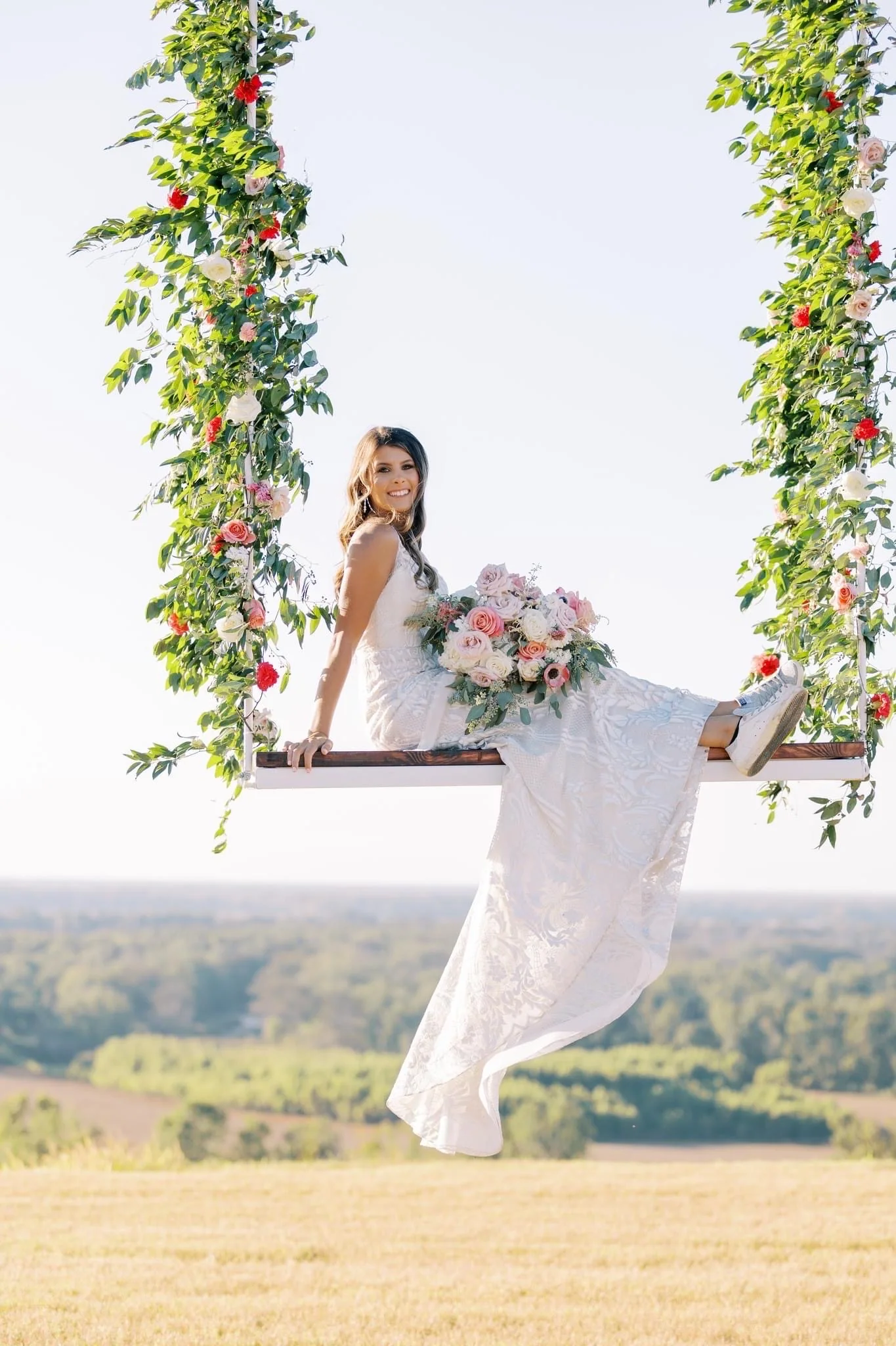 Bride seated on a flower-wrapped swing overlooking the countryside