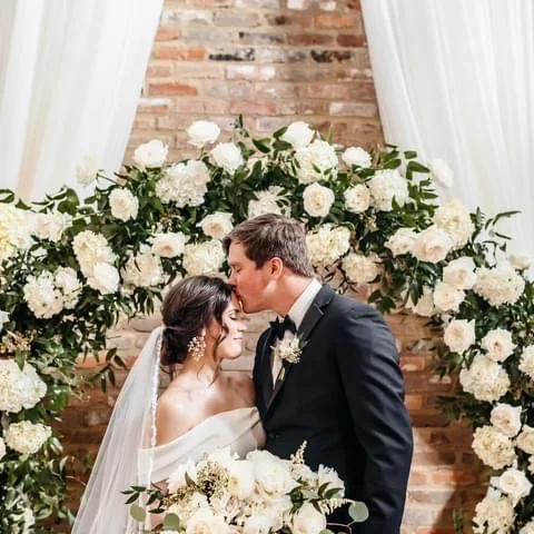 Newlyweds beneath a white floral ceremony arch