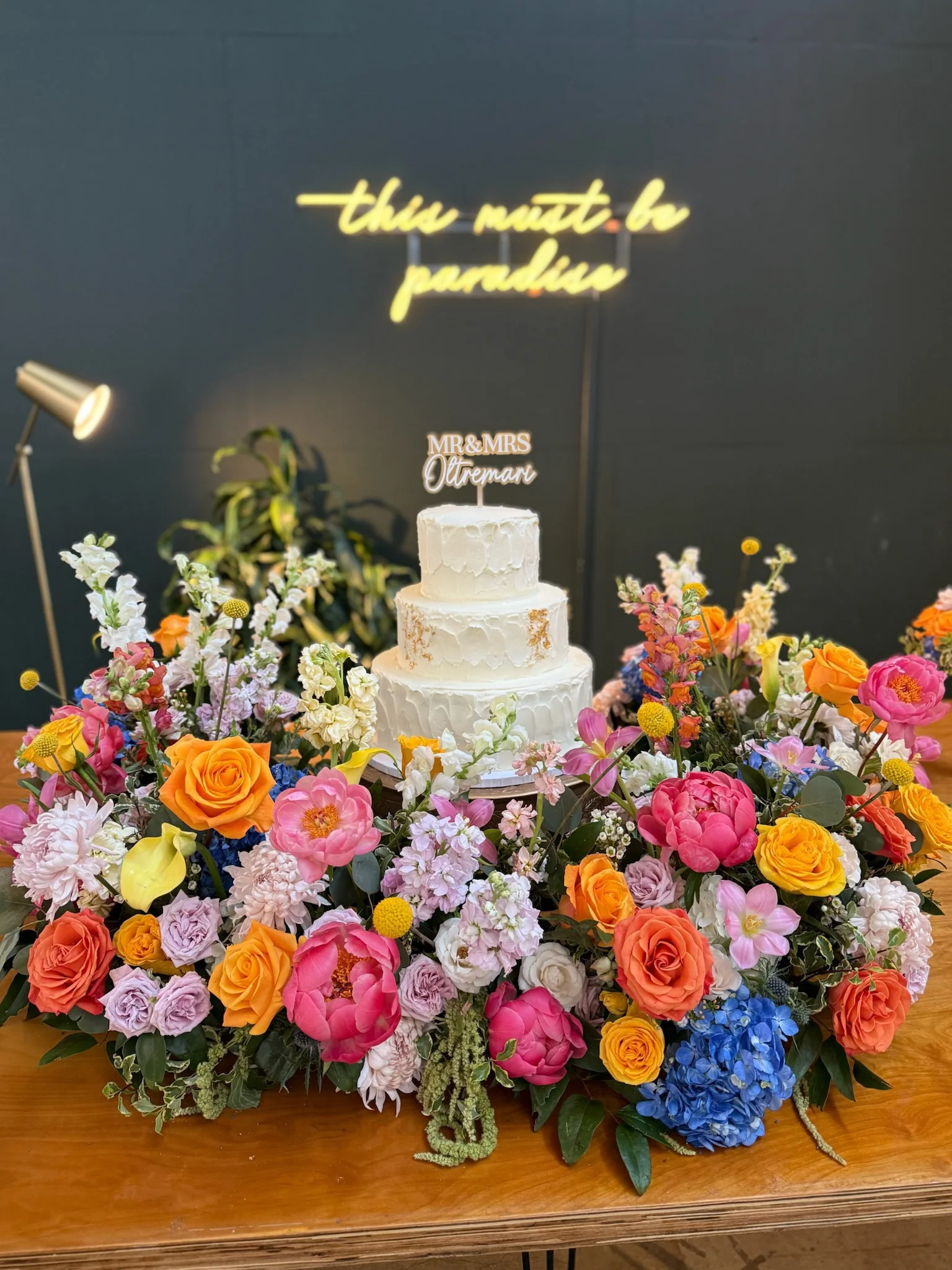 Colorful floral arrangement surrounding a white wedding cake